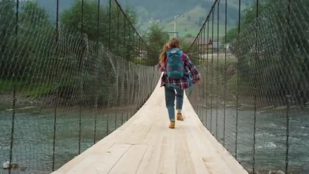 Pendaki wisata yang bersemangat berjalan di jembatan sungai. Wanita bahagia melompat di pegunungan. — Stok Video