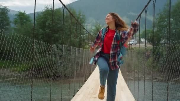 Glücklicher Reisender, der auf Flussbrücke Berge hüpft. Emotionale Frau geht auf Wanderschaft. — Stockvideo
