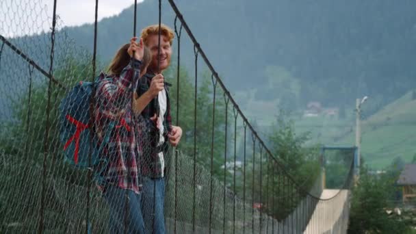 Pozitivní pár stojící most v horách. Venku spolu mluví dva turisté.. — Stock video