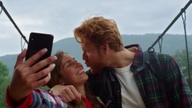 Eğlenceli aşıklar akıllı telefon özçekim seyahat blogunda fotoğraf çekerler. Dağlarda çift öpüşmesi.