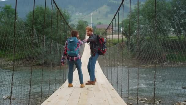 Backpackers stående flodbro på fjällvandring. Lyckligt par leker. — Stockvideo