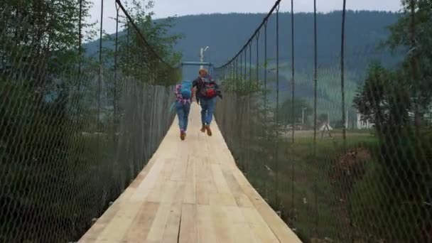 Friends run racing outdoors on mountains bridge. Tourists wear backpacks on hike — Stock Video