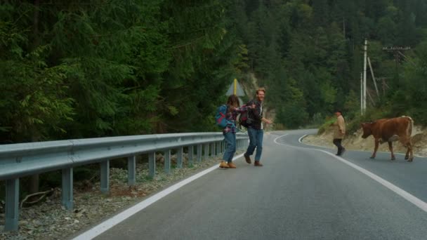 여름에는 히치 하이킹을 하는 사람들 이 산악 도로를 따라 걷습니다. 도로에서 차를 타고 있는 부부. — 비디오