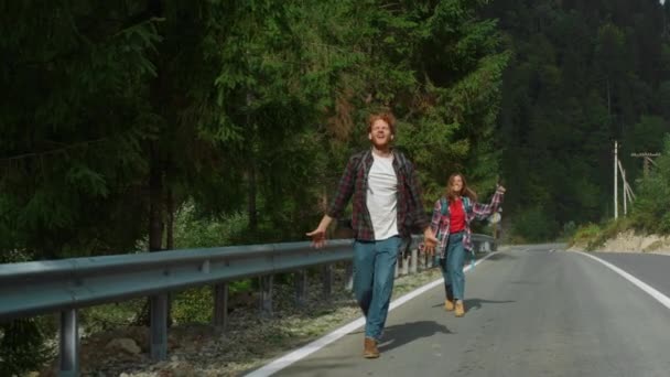 Überglückliche Tramper winken auf der Bergstraße. Paar springt auf Autobahn. — Stockvideo