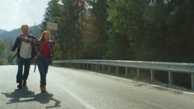 Dağlarda bir çift orman yolunda yürüyor. Otostopçular dışarıda el sallamayı bekler.