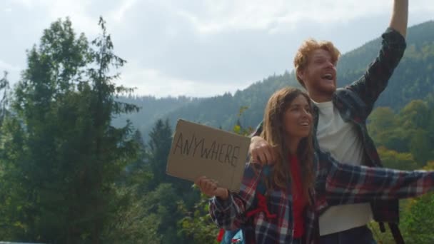 Milující pár stopování přírody na horské silnici. Cestovatelé drží plakát. — Stock video