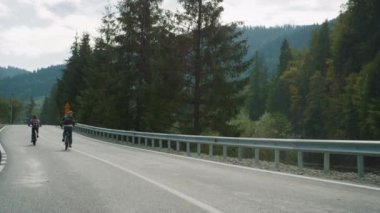 Yaz ormanlarında bisikletçiler dağ manzarası çizerler. Arkadaşlar yolda bisiklet sürer.