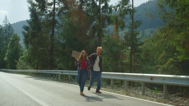 HItchhikers promenader skog vägkanten i bergen. Par resenärer som håller skylt. — Stockvideo