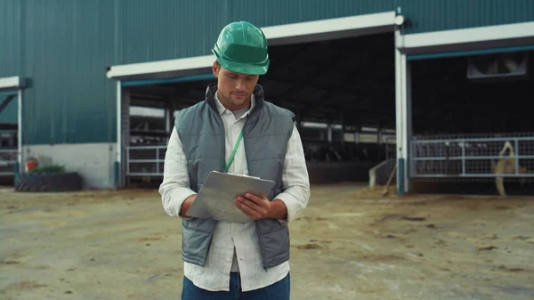 Supervisor engineer holding clipboard making notes at modern cowshed building. — Foto de Stock