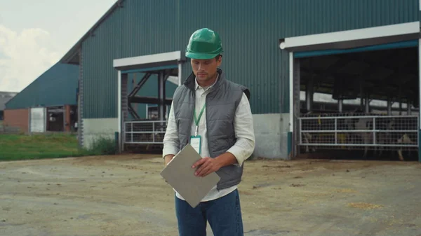 Livestock supervisor making notes holding clipboard at modern cowshed building. — Foto de Stock
