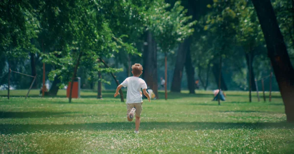 Energetische Grundschulkinder laufen an sonnigen Tagen auf einer grünen, saftigen Wiese. Kamera-Zoom. — Stockfoto
