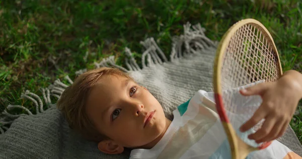 Closeup chateado menino examinando raquete badminton de madeira deitado grama verde sozinho — Fotografia de Stock