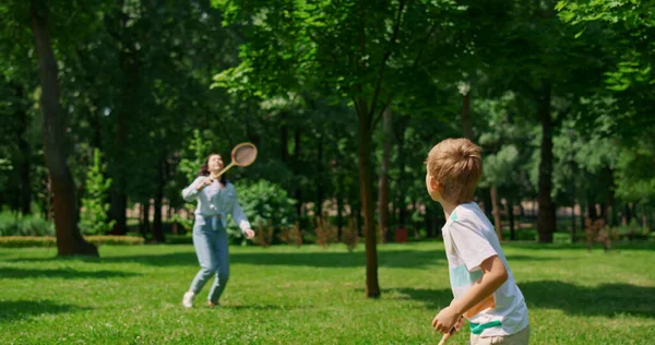 Aktiv pojke spelar badminton med mamma i bakgrunden. Begreppet idrott i familjelivet — Stockfoto