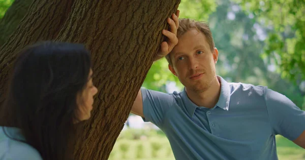 Homem calmo conversando com a esposa se inclina na árvore de perto. Retrato de família em repouso — Fotografia de Stock