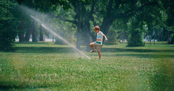 Verspielter Junge im Grundschulalter, der Wassersprenger-Strahl tritt. Kind genießt Zeit im Park — Stockfoto