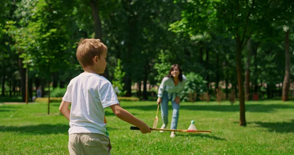Fröhliche Mutter spielt Badminton mit Sohn im Park. Glückliche Familie hat Spaß im Freien. — Stockfoto