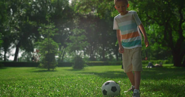 Aktywny chłopiec kopać piłkę na zielonej trawie. Mały sportowiec grać w piłkę nożną w parku. — Zdjęcie stockowe