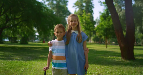 Två leende syskon poserar med racketar. Lekfulla barn kramas i parken. — Stockfoto