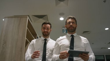 Ofis çalışanları ofis koridorunda dijital tablet bilgisayar kullanarak iş konuşuyorlar