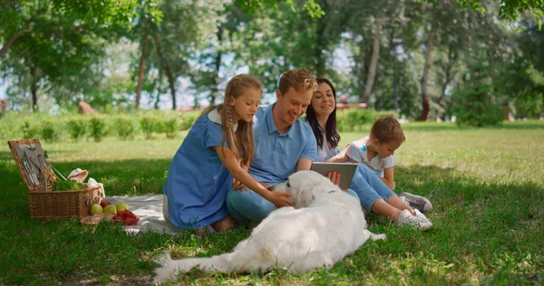 Happy family use tablet on picnic. Parents watching laptop with two kids outside — Stock Photo, Image