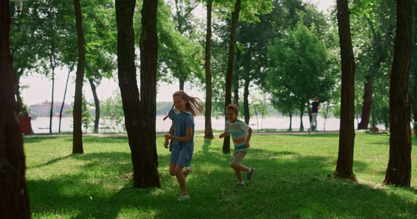 Riendo niños corriendo en el soleado prado. Los niños felices juegan a ponerse al día en el parque. —  Fotos de Stock