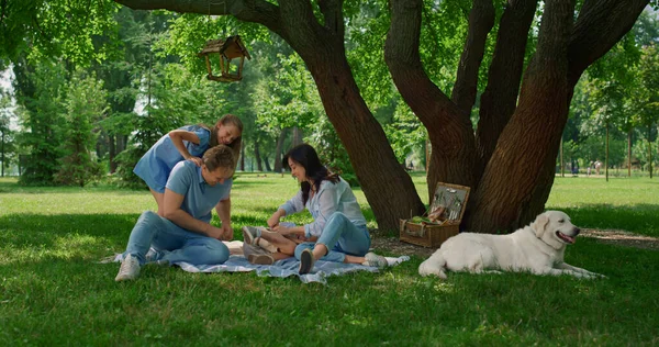 Skrattande familj har roligt spel på picknick filt. Lyckliga människor vilar utanför. — Stockfoto