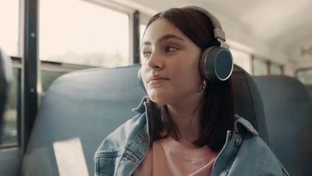 Tonårstjej njuter av att lyssna musik med hörlurar sittande buss på nära håll. — Stockvideo