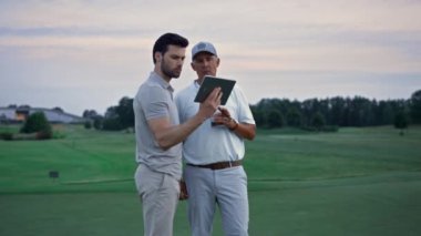 Golf sahasında gün batımında tablet seyreden iki golfçü..