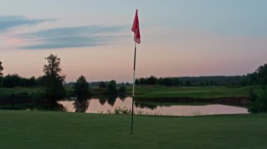 Golf sahasında kırmızı bayrak var. Flagstaff boş yeşil rota gün batımında.