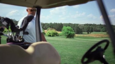 Golf arabasına doğru yürüyen lüks bir golfçü. Zengin adam golf kulübünde at arabasında oturuyor..