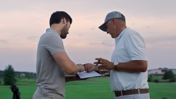 Les hommes de golf signent le contrat de document sur le terrain de golf. Deux hommes d'affaires font affaire. — Video