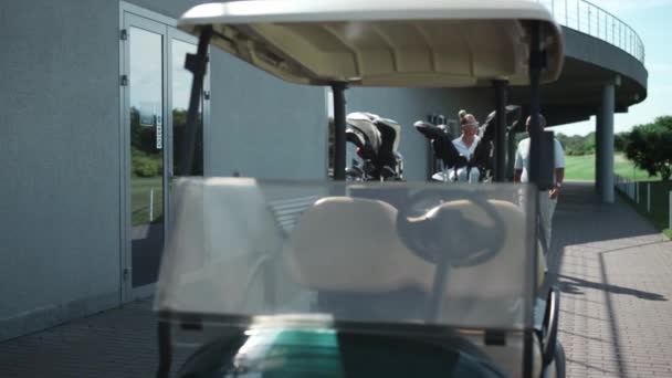 裕福なカップルゴルフ運転カートにコースを歩く。スポーツチームはカントリークラブを楽しむ. — ストック動画
