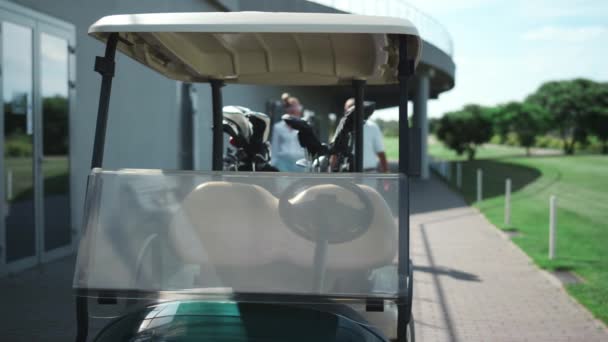 ゴルフプレーヤーは外に準備ができてカートに座る。アクティブカップルはコース上で車を運転します — ストック動画