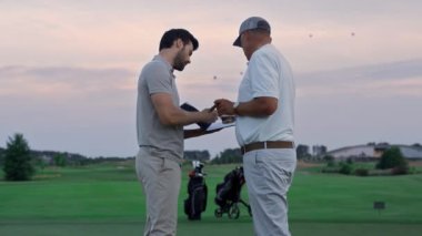 Golfçüler yeşil sahada anlaşırlar. Erkekler belge kağıtlarını dışarıda imzalıyorlar