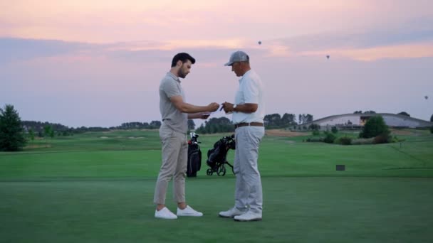 Два бизнесмена стоят снаружи на поле для гольфа. Спортсмены подписывают бумаги на поле. — стоковое видео