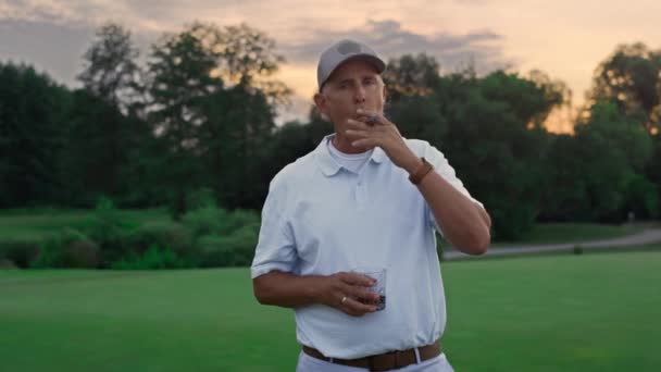 Bohatý golfista se na hřišti uvolnil. Starý muž kouří doutník s pitím. — Stock video