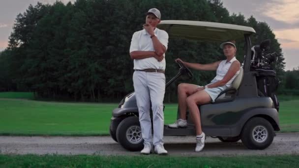 Golfspelers zitten op koers. Sport paar genieten van de activiteit in het besturen van golf auto — Stockvideo