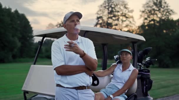 Bohatý pár si užije golfový večer na fairwayi. Rodinní golfisté relaxovat letní dovolenou. — Stock video