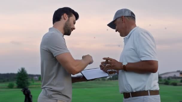 两名高尔夫球手在日落球道外进行交流.高尔夫团体穿运动服谈话 — 图库视频影像