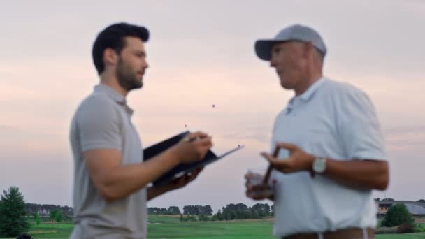 Dos hombres hablando de campo de golf afuera. Los golfistas analizan el resultado del juego al atardecer — Vídeo de stock