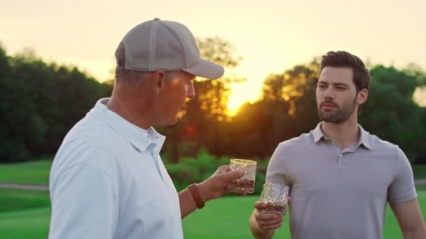 Dos golfistas charlando juntos en el campo verde. El equipo de golf bebe whisky afuera.. — Vídeos de Stock