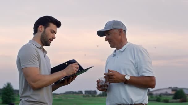 Zespół golfowy czatujący przyjazny na zachodzie słońca pole golfowe. Dwóch mężczyzn uścisnęło sobie dłonie. — Wideo stockowe