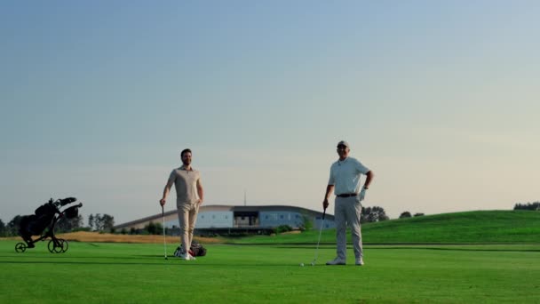 两个男人喜欢在球道球杆上打高尔夫 高尔夫球队在日落赛程上练习运动 重点教练组使用推杆球外击球 高尔夫球手喜欢大自然的游戏 主动概念 — 图库视频影像