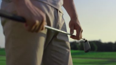 Golf oyuncusu gün batımı sahasında golf sopası sallıyor. Golfçü spor maçına vurgu yapıyor. Pist sahasında elinde golf malzemesi tutan tanınmamış bir adam. Lüks hobi zengin yaşam tarzı aktivite konsepti.