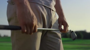 Gün batımı sahasında golf sopası tutan golfçü elleri. Adam açık havada golf oynamayı seviyor. Kırsal alanda oynanan maçta golf ekipmanı kullanan bilinmeyen bir profesyonel kulüp üyesi. Etkinlik kavramı.