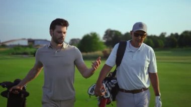 Yakışıklı golfçüler spor hobisi konuşuyor. Aktif adamlar dışarıda golf sopaları taşırlar. Başarılı profesyonel golfçüler hafta sonları yeşil çimlerde yürürler. Sporcular bir arada.