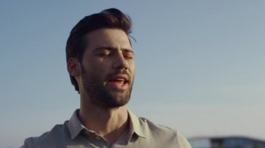 İnsan yüzü doğanın mavi gökyüzüne bakar. Güneşli yaz gününde gülümseyen seksi sakallı adamın portresi. Neşeli erkek model dışarıda gülüyor. Genç işadamı tatilin tadını çıkarıyor. Keyif konsepti..