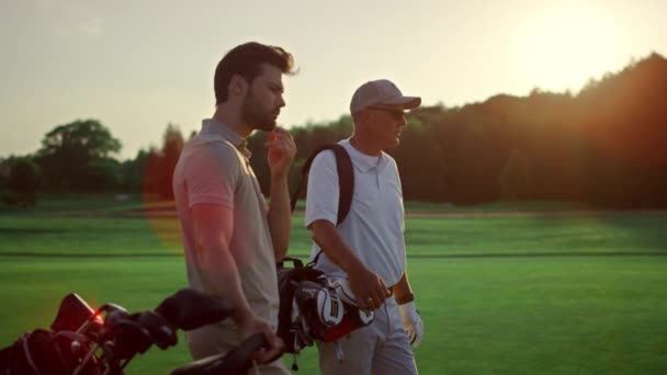 富人在夕阳西下的夏季高尔夫球场打高尔夫球 两名运动员在场上玩体育 职业高尔夫球手队伍在乡村俱乐部中遥遥领先 积极的团体站在运动服上 文娱活动概念 — 图库视频影像