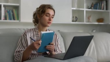 Yakın plan genç iş kadını evdeki online konferansı izlerken notlar alıyor. Odaklanmış öğrenci not defteriyle uzaktan yazarak ders çalışıyor. Güzel bayan ev hanımı dinleniyor. Hafta sonları yemek bloğunun keyfini çıkar.