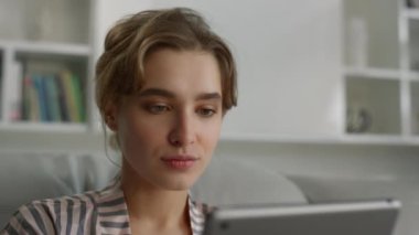 İnternette internette gezinen, oturma odasında dudaklarını ısıran ciddi bir kadın. Çekici iş kadını, elinde dijital tablet bulunan çalışana odaklanmış. Güzel bayan, sosyal medyayı kontrol et